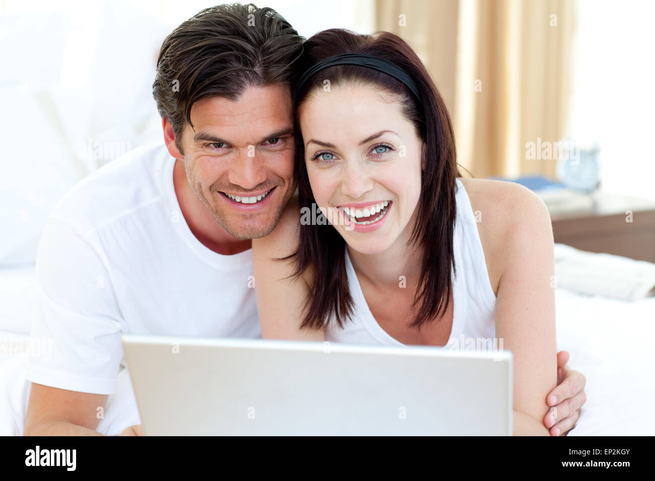 Smiling couple using a laptop lying on their bed Stock Photo - Alamy