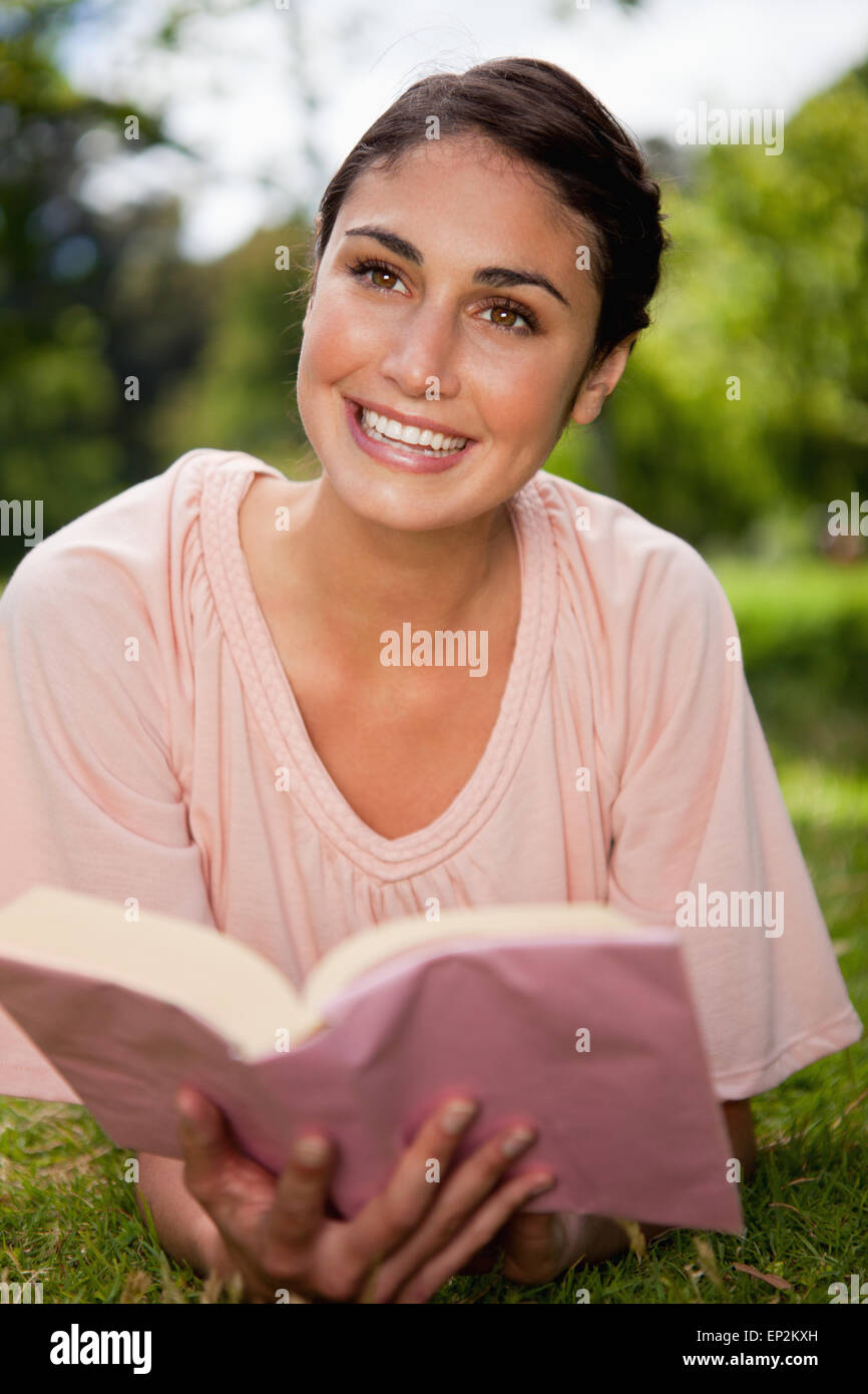 Woman looks upwards while reading a book as she is lying down Stock