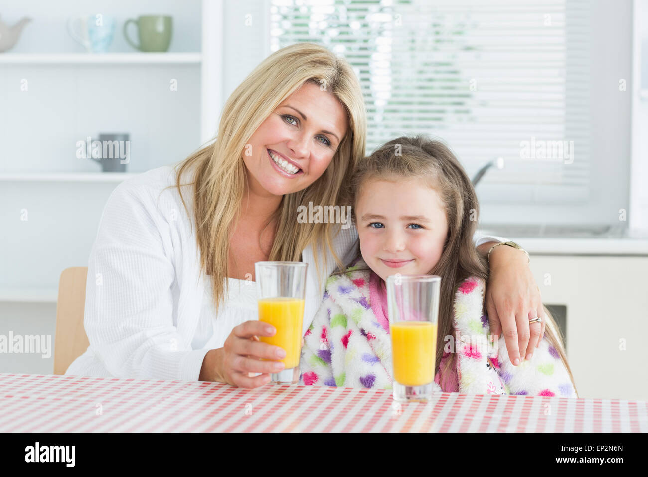 Woman and little girl sitting at the kitchen having juice Stock Photo