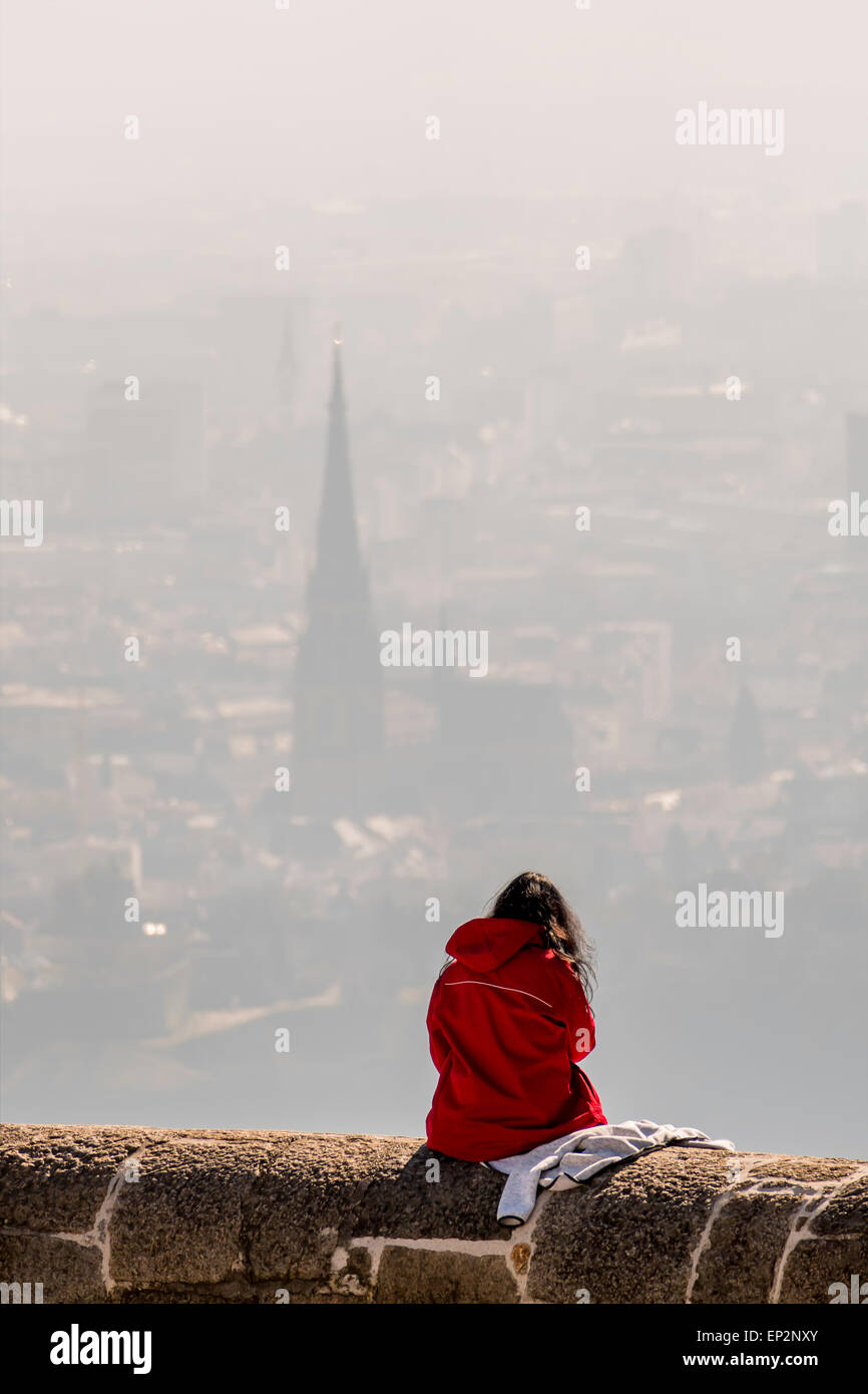 Austria, Linz, woman sitting on wall of Poestlingberg looking at town Stock Photo