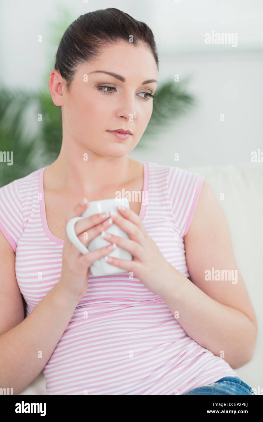 Thoughtfully woman sitting on the couch holding a mug Stock Photo