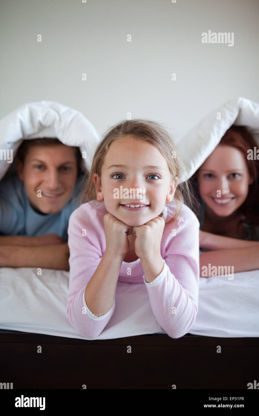 Smiling girl under bed cover with her parents Stock Photo Alamy
