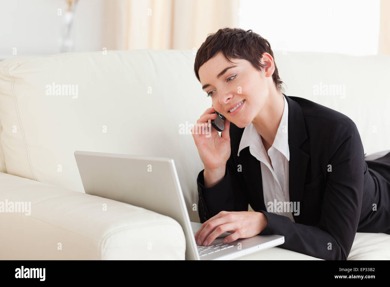 Smiling Woman lying on a sofa with a laptop and a phone Stock Photo - Alamy