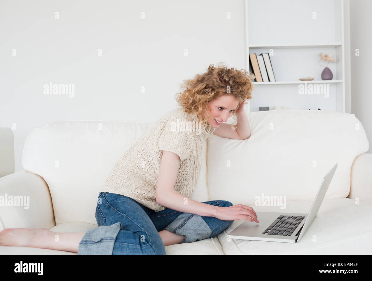 Pretty blonde woman relaxing with her laptop while sitting on a sofa ...