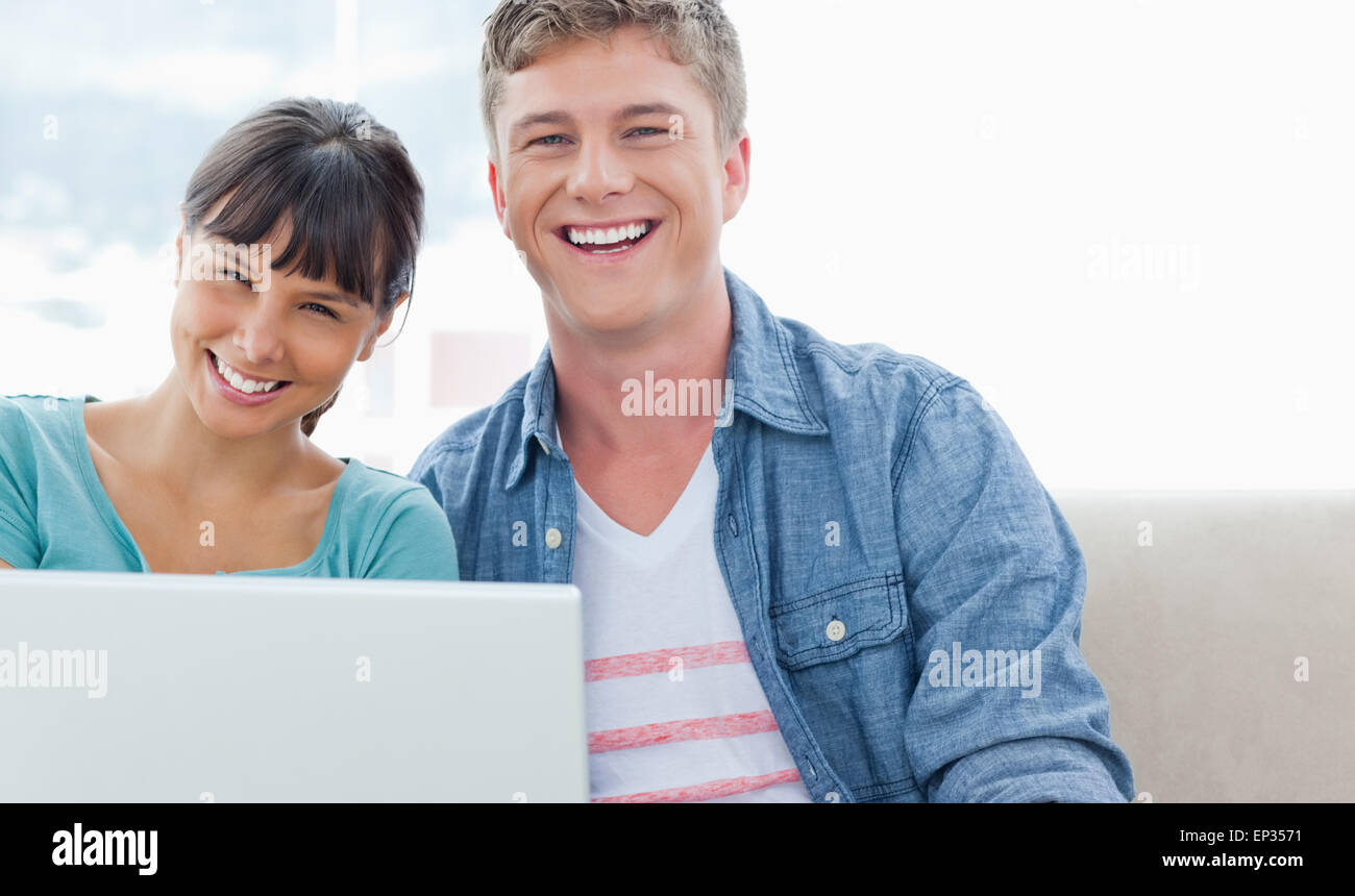 A laughing couple sitting on the couch with a laptop as they look into ...