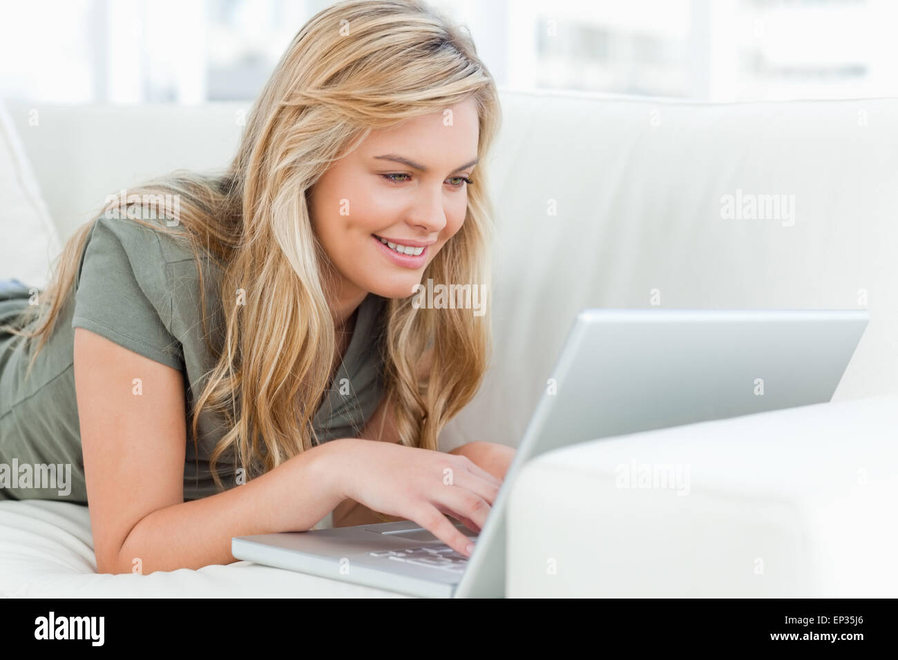 Woman lying across the couch using her laptop and smiling Stock Photo ...