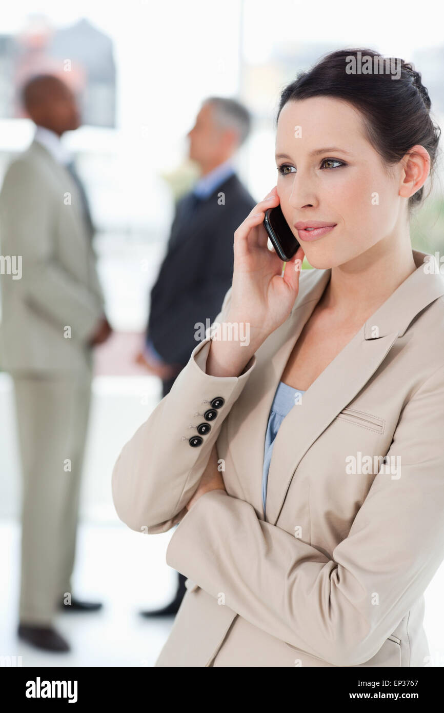 Businesswoman seriously talking on the phone with executives behind her Stock Photo
