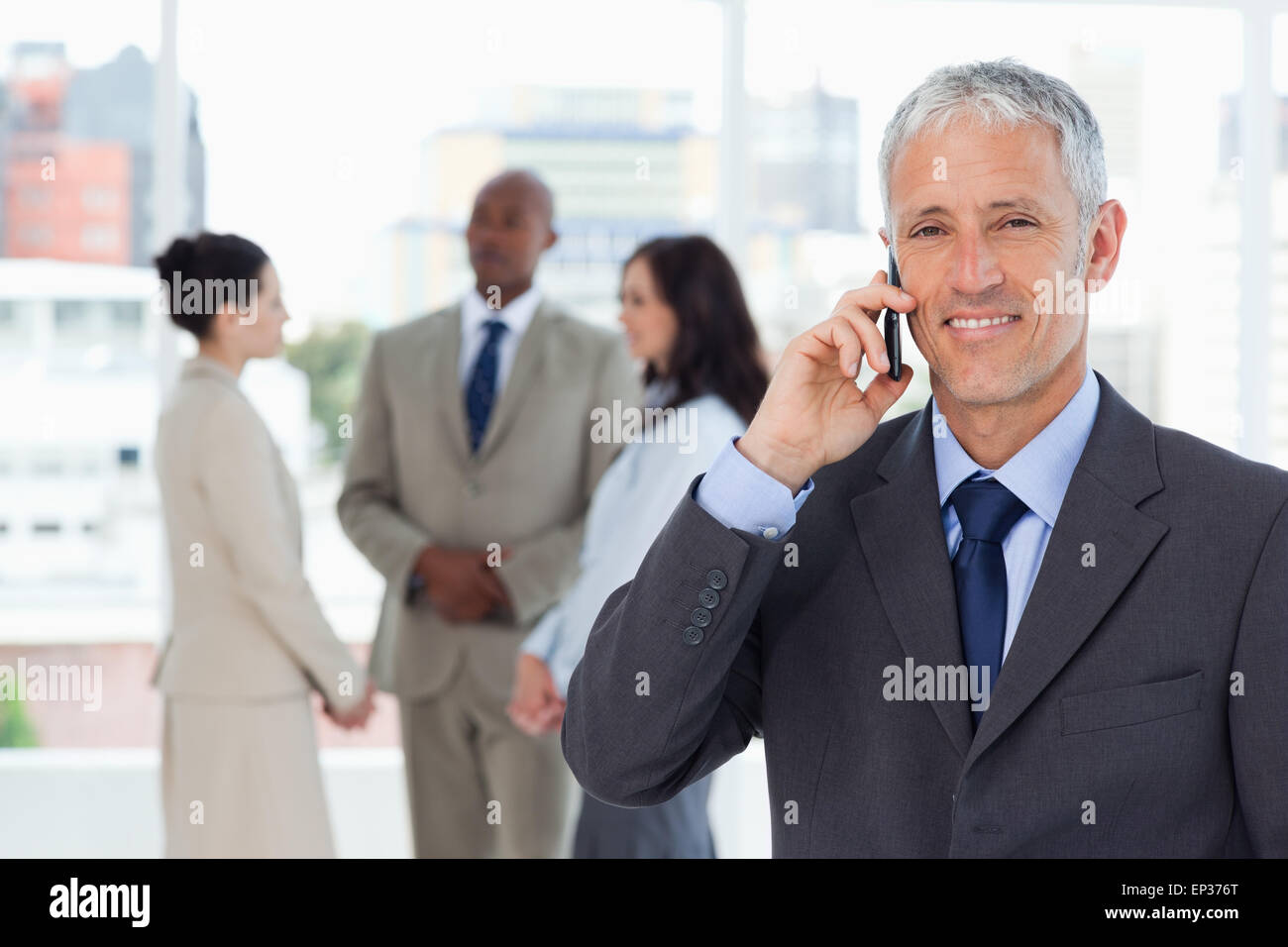 Smiling manager talking on the mobile phone while his team is behind ...