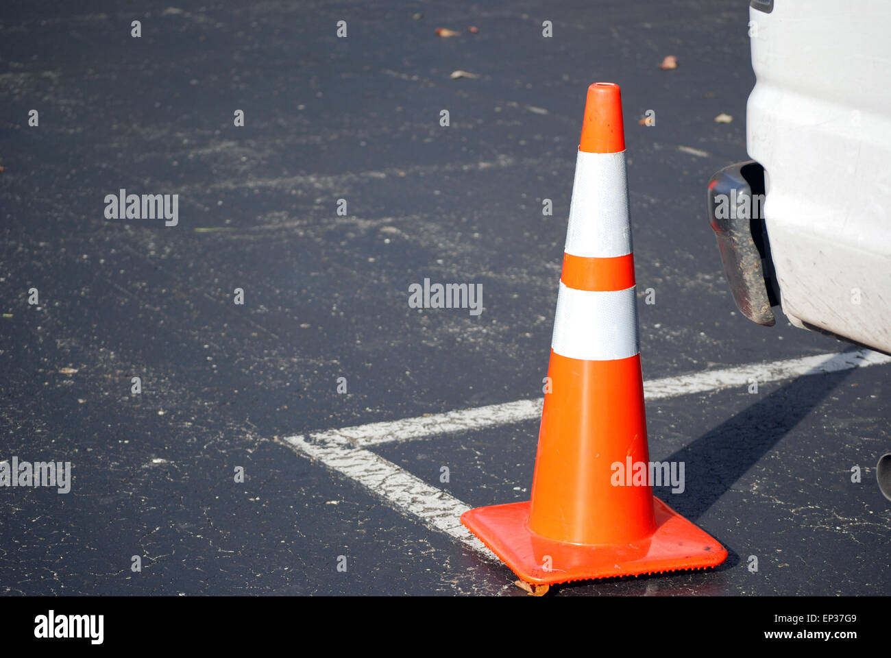 Bright orange traffic cone by rear bumper of a white truck in parking lot. Stock Photo