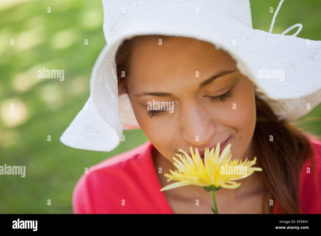 Woman wearing a white hat while smelling a flower with her eyes closed ...
