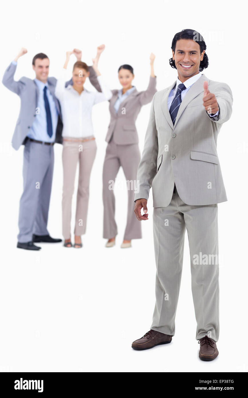 Businessman smiling with his thumbs up and cheering people behind him ...