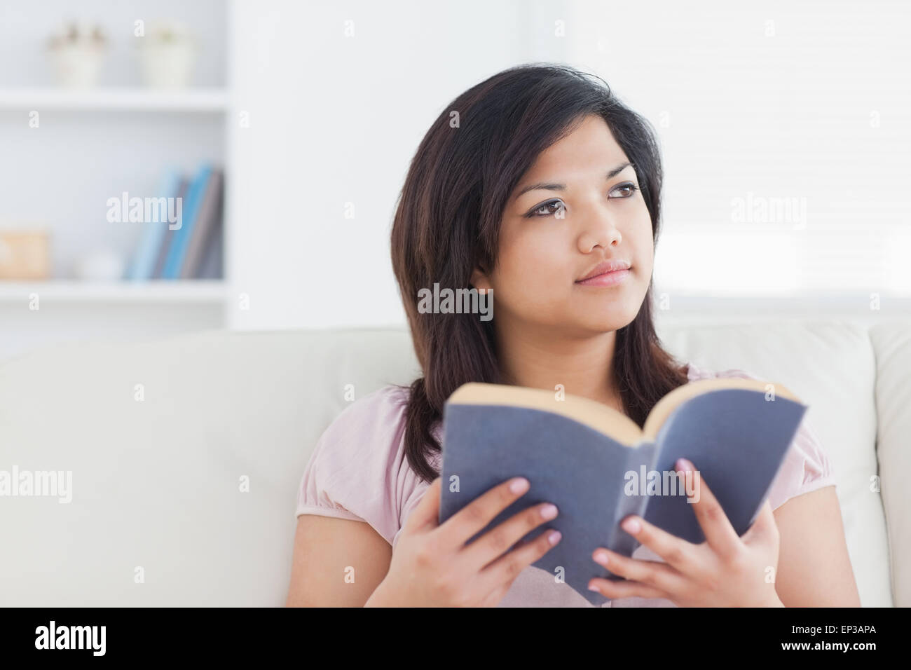 Woman sitting on a sofa while holding a book Stock Photo - Alamy