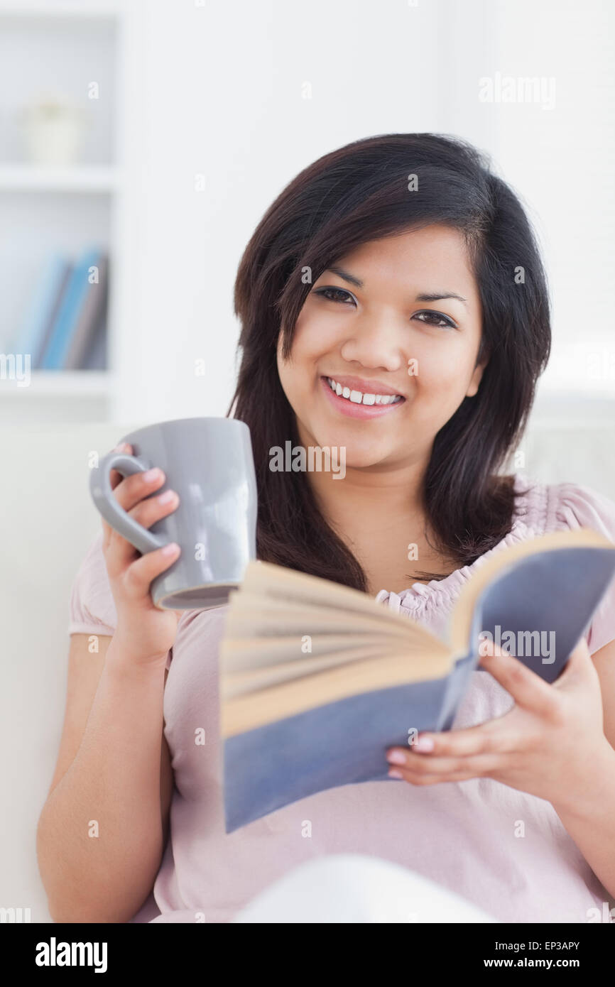 Woman smiling while holding a mug and a book Stock Photo - Alamy