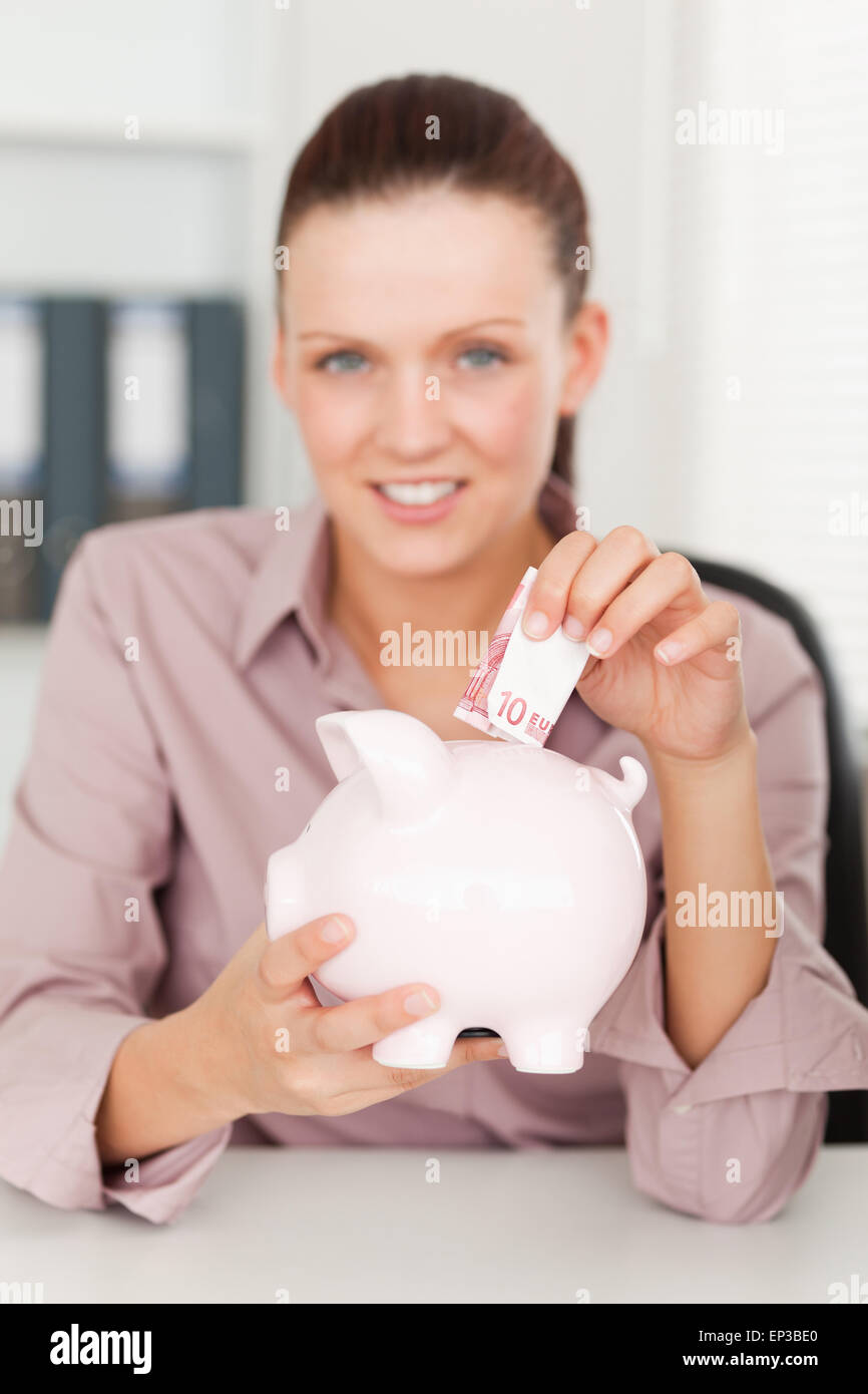 Businesswoman putting money into piggy bank Stock Photo - Alamy
