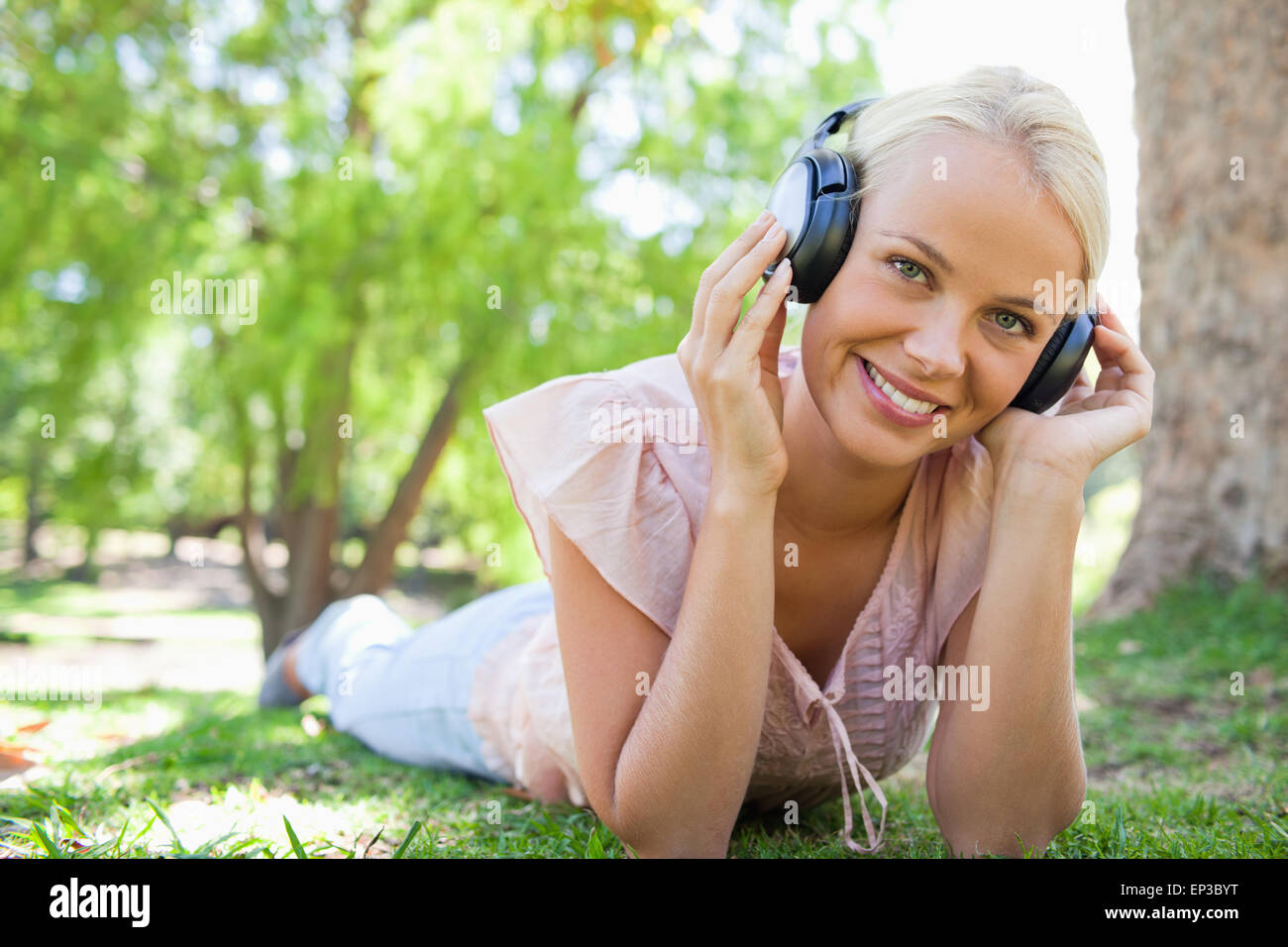 Smiling woman lying on the grass while listening to music Stock Photo ...