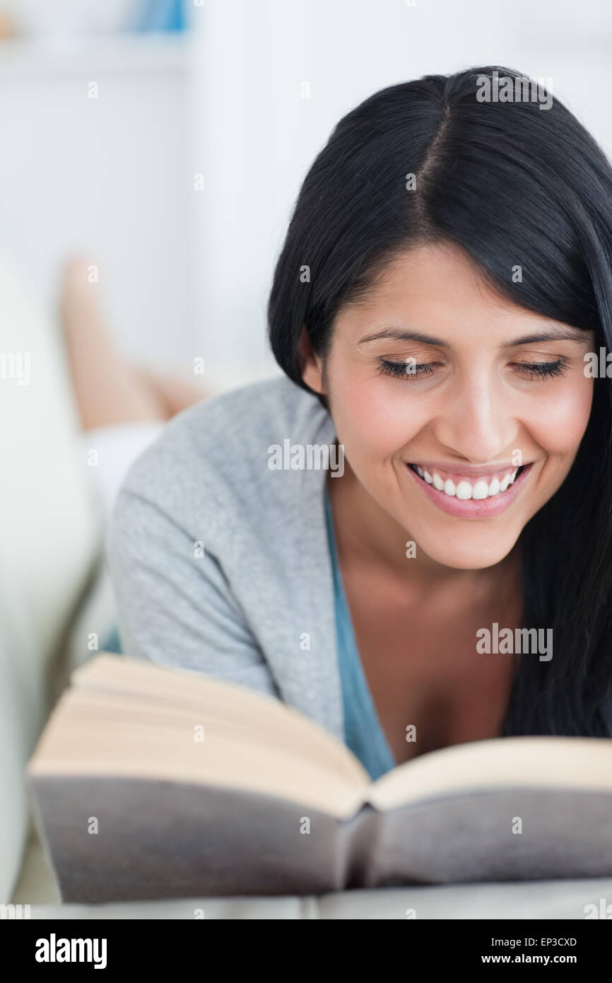 Woman smiling while reading a book as she lies on a couch Stock Photo