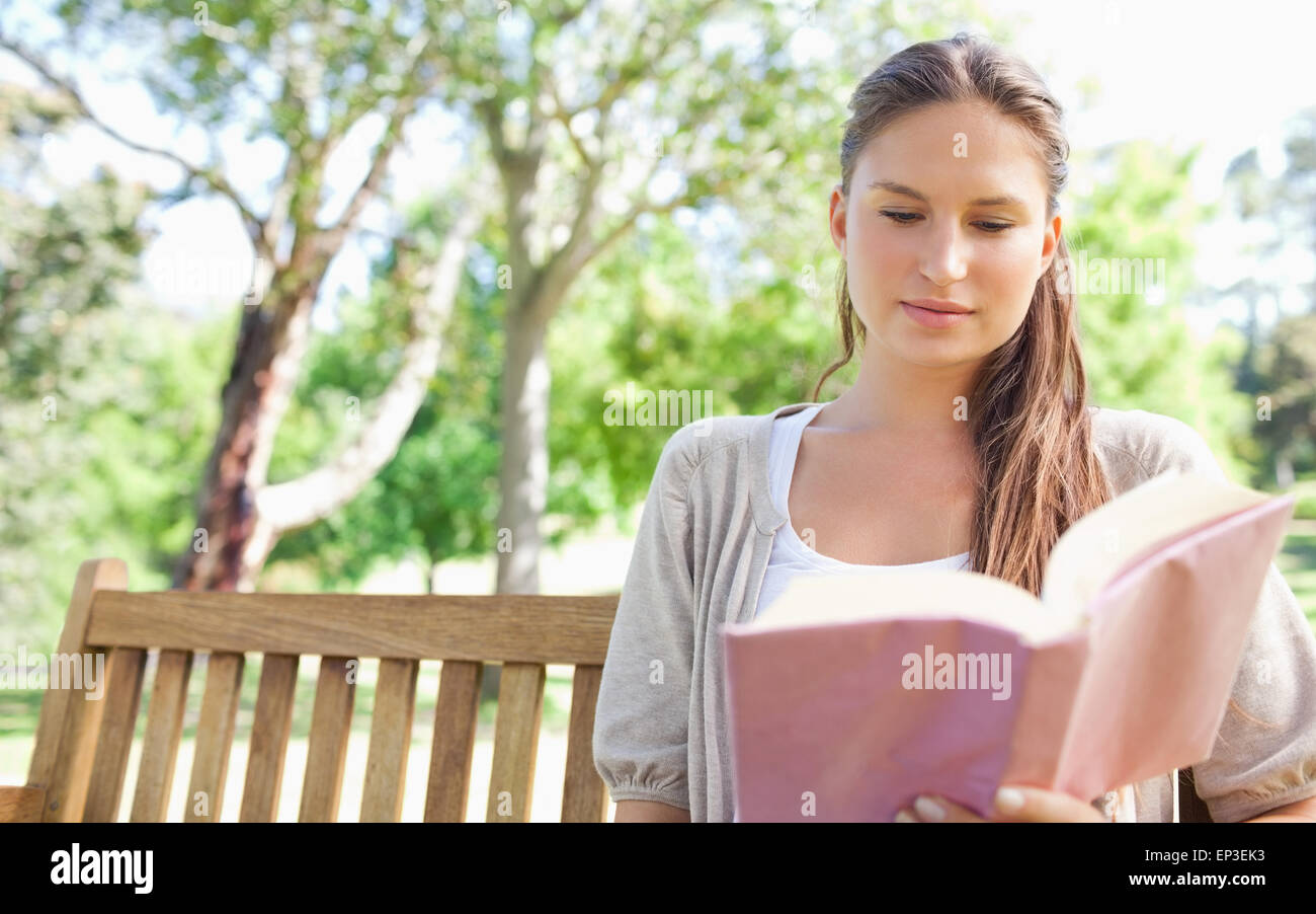 Woman sitting on a park bench while reading a book Stock Photo - Alamy