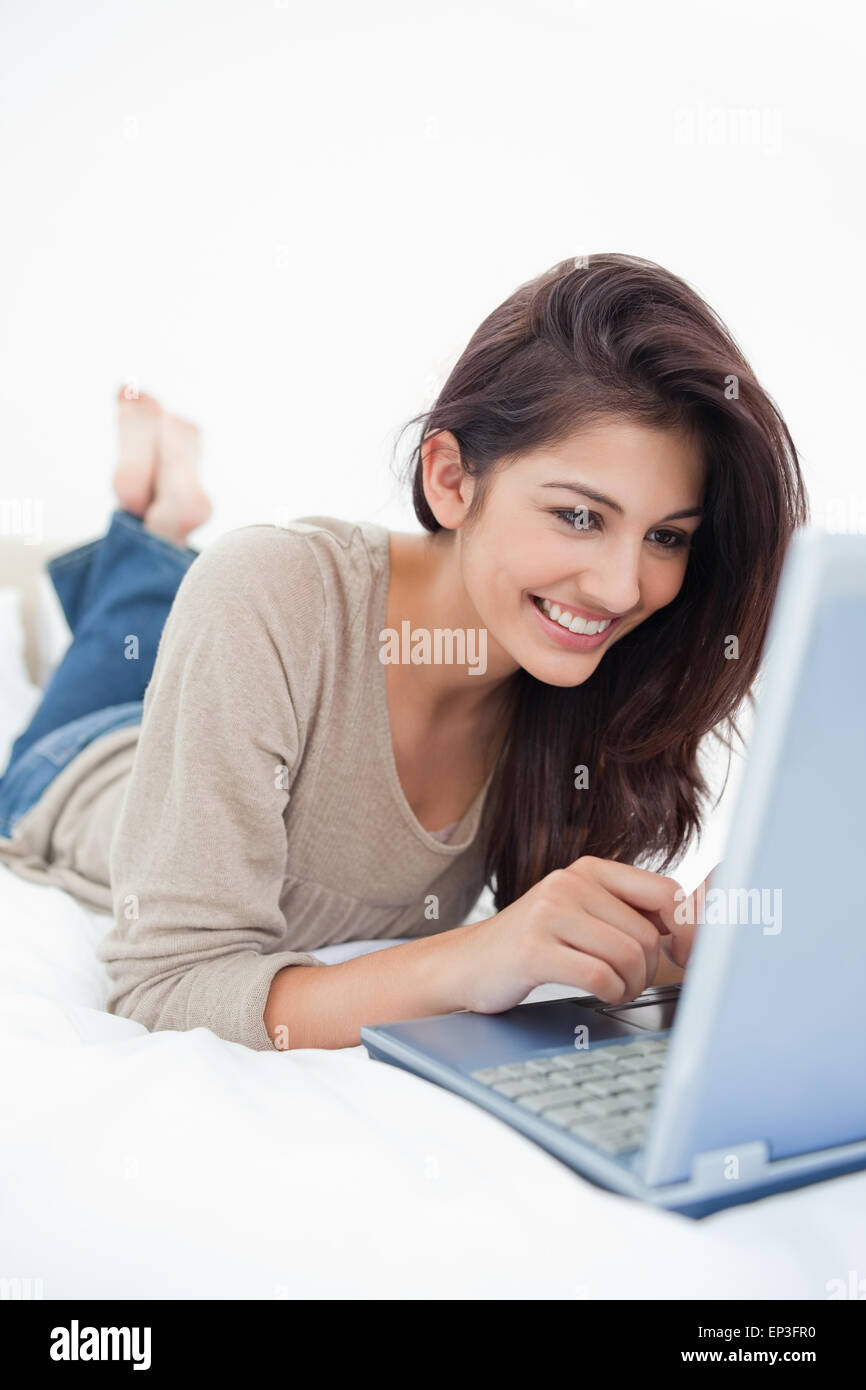 Close up, woman lying on the bed smiling with her laptop in front of ...