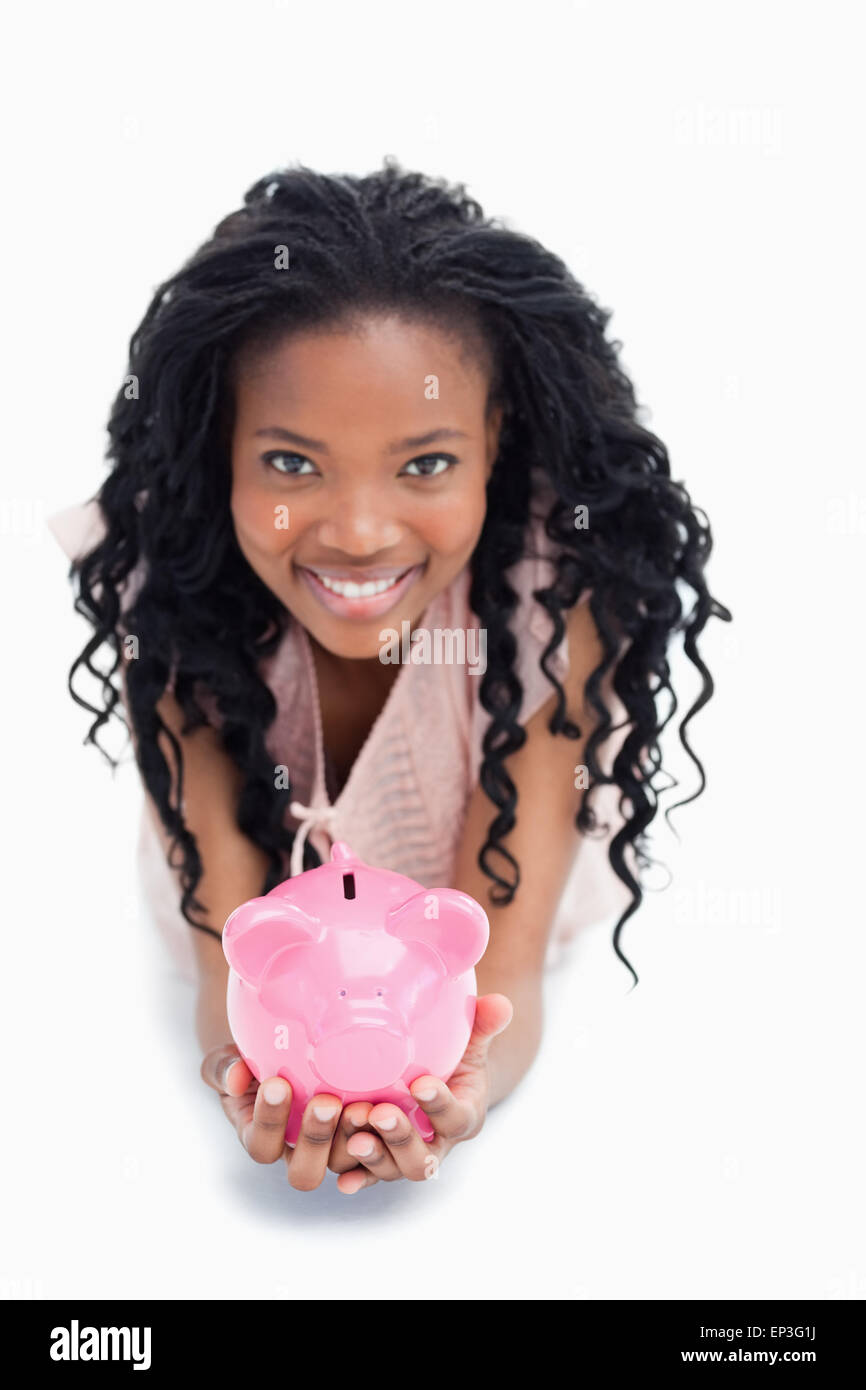 A young woman smiling at the camera is holding a piggy bank in her ...