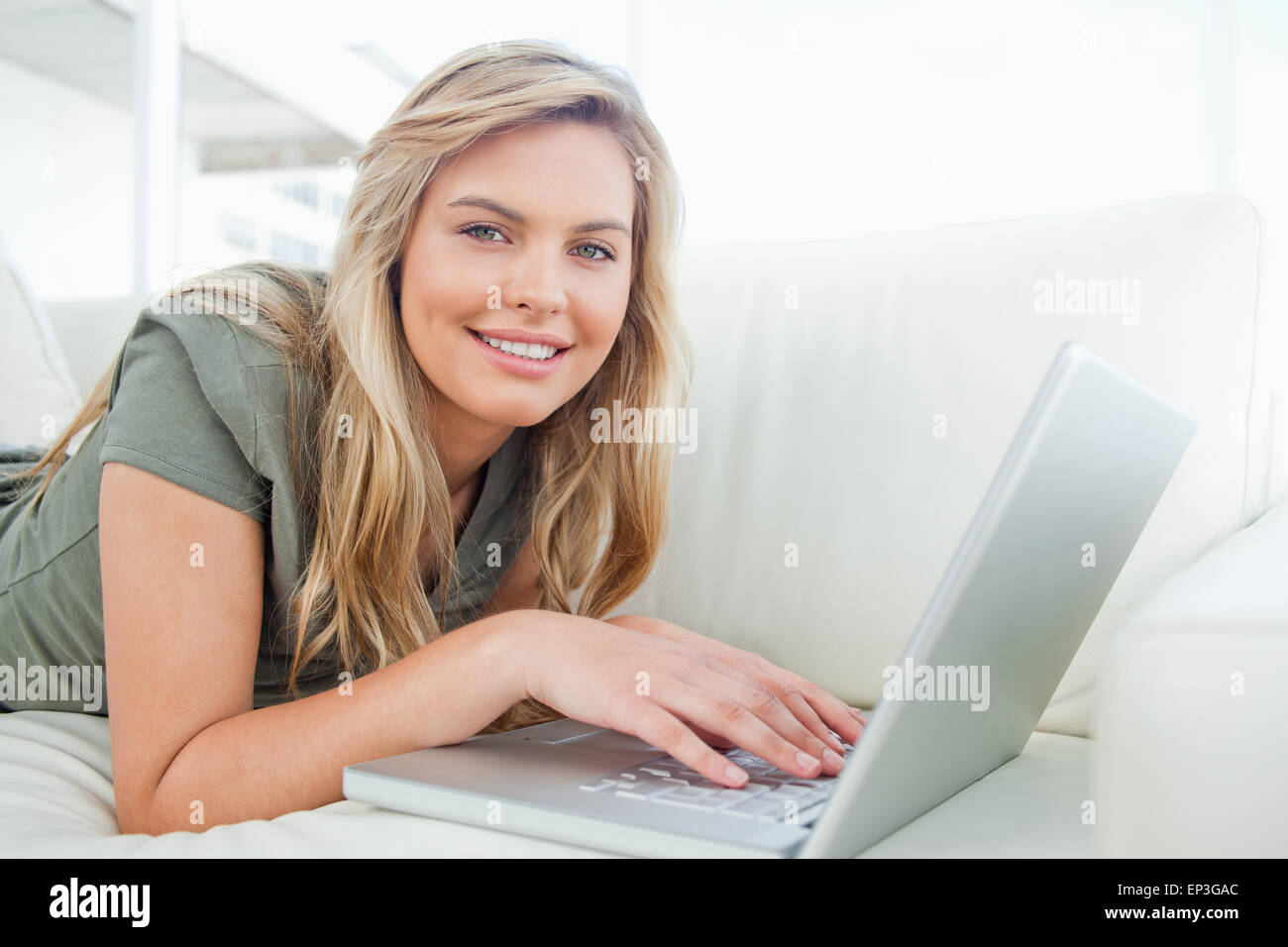 Woman looking ahead, smiling as she uses her laptop while lying on the ...