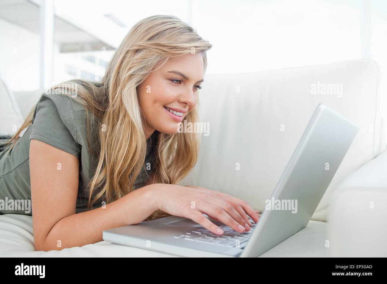 Woman smiling as she uses her laptop while lying on the couch Stock ...