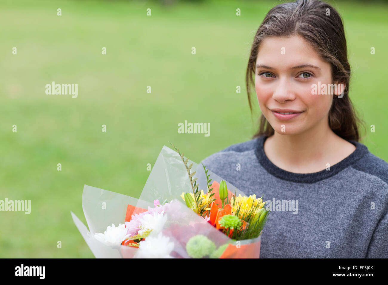 Young calm girl holding a bunch of flowers while standing in a park ...