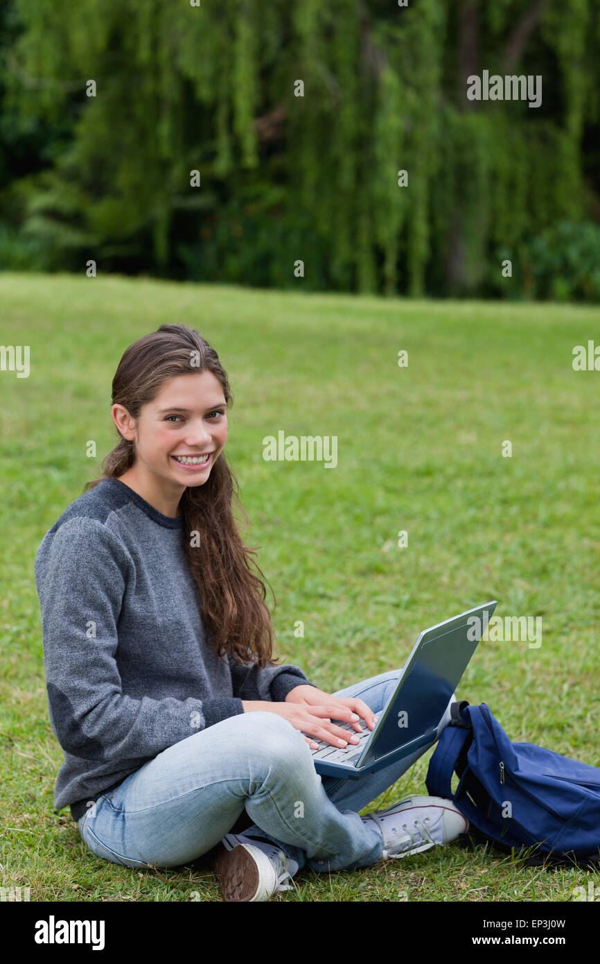 Young woman sitting cross-legged on the grass while using her laptop ...