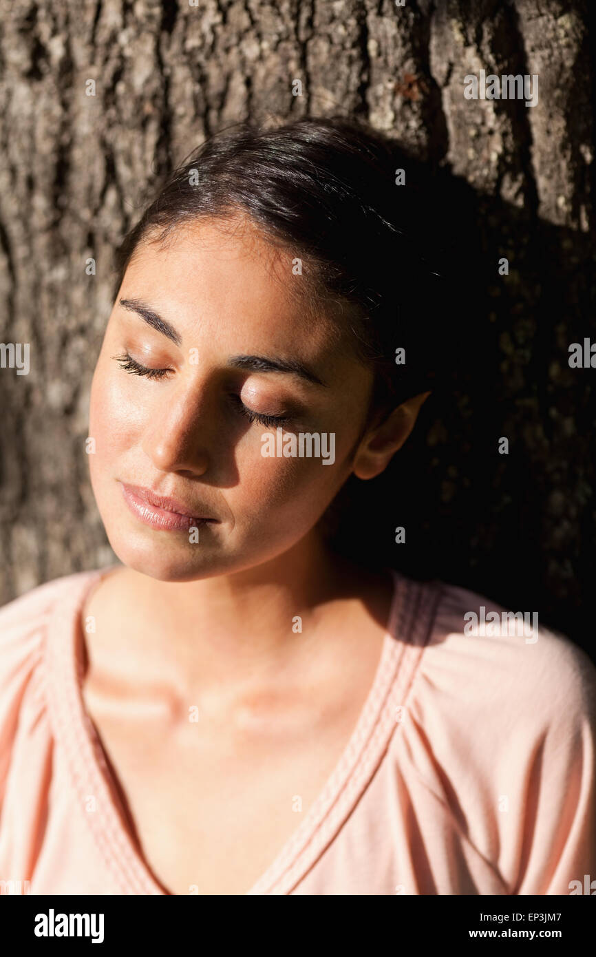Woman closing her eyes while sitting against a tree Stock Photo - Alamy