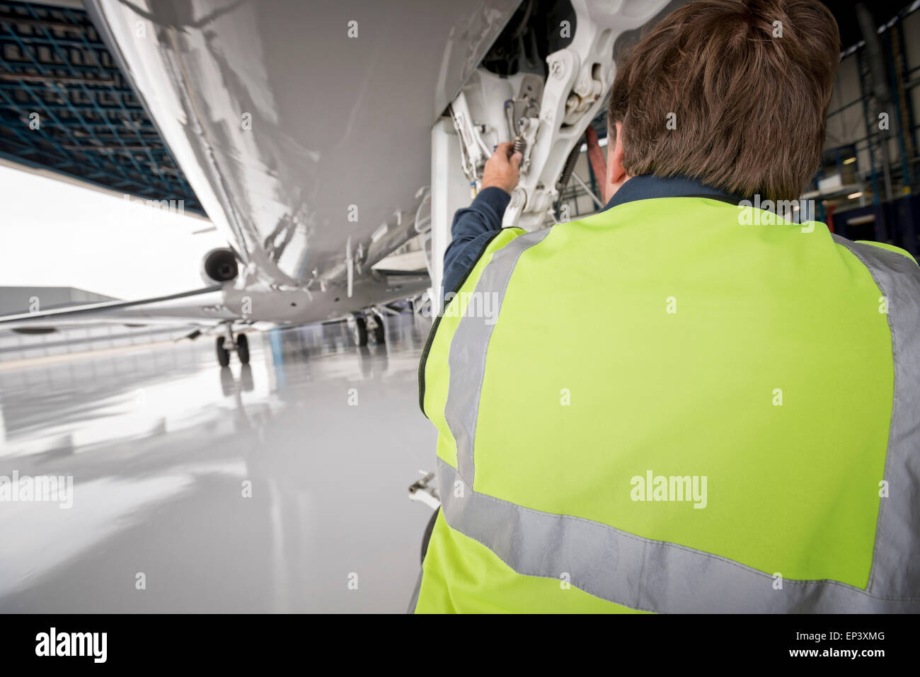 Mechanic in yellow Hi Viz inspecting the nose landing gear of a jet airplane in a hanger Stock Photo