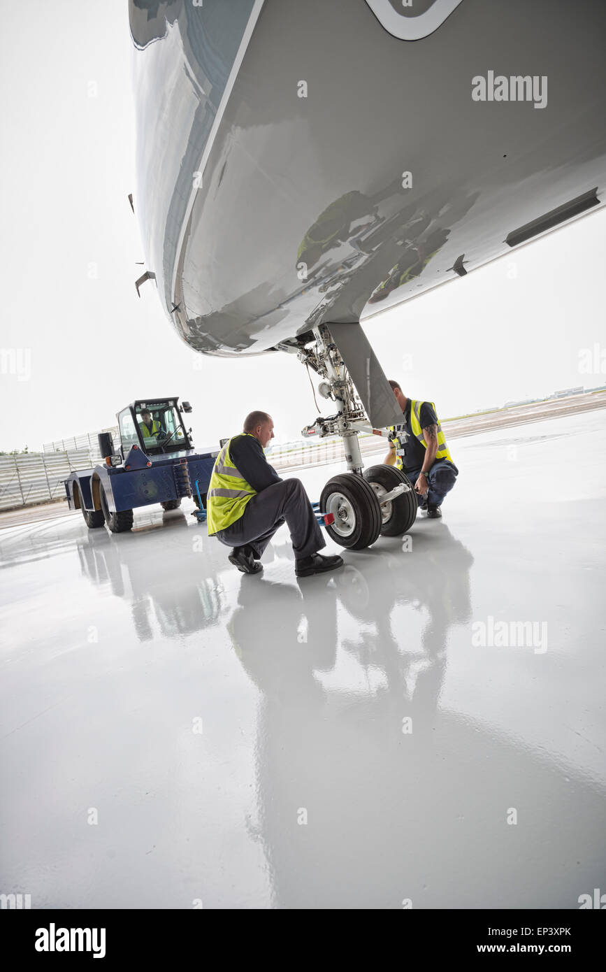 Ground crew attaching a tow bar to an aircraft's nose landing gear with