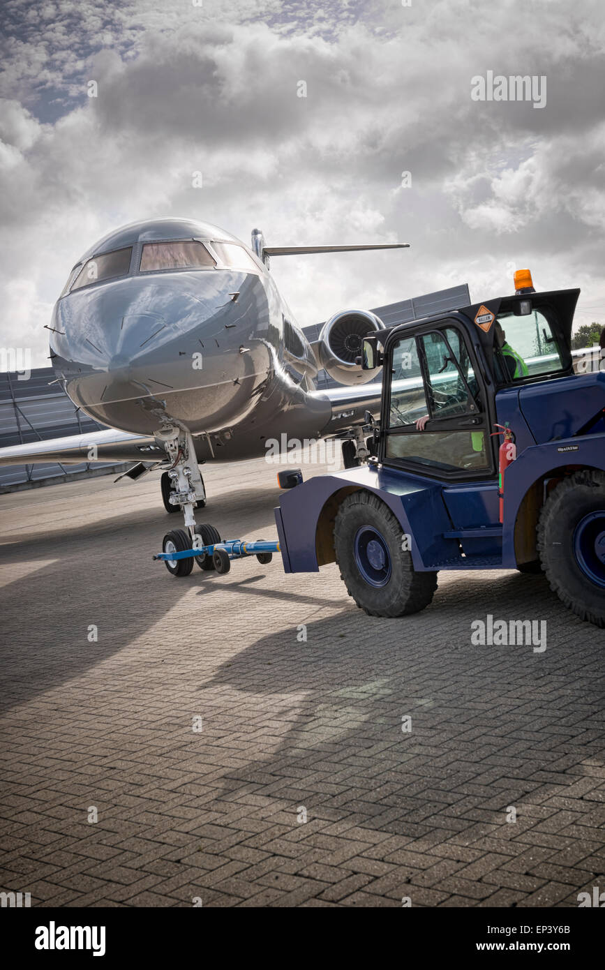 Airplane being pushed back by a tractor with a tow bar connected to the nose landing gear Stock Photo