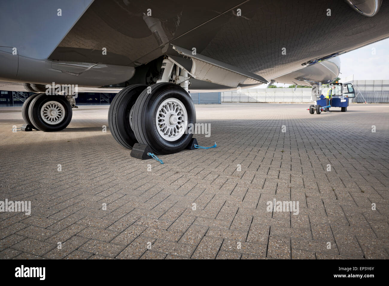 Wheel chocks deployed on an airplanes landing gear as the aircraft is prepared to be pushed back by a towing tracktor Stock Photo