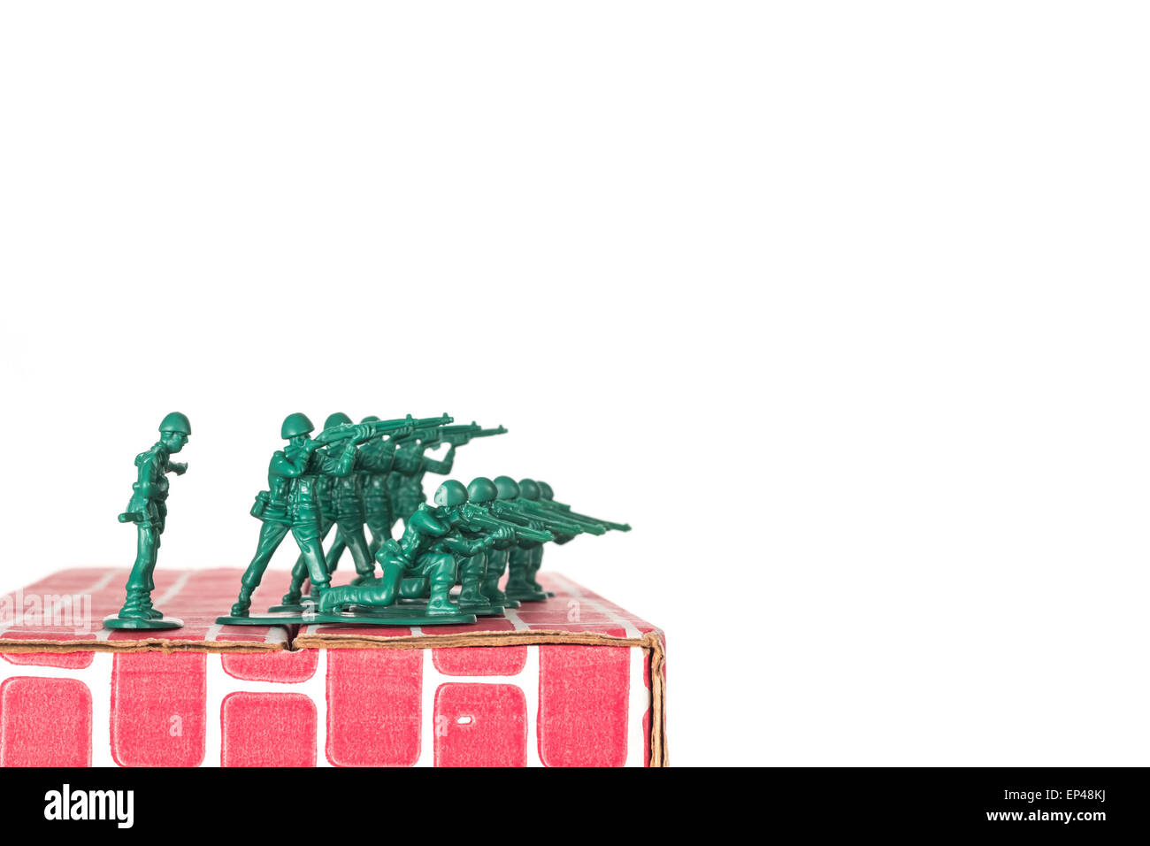 Green army men guarding the top of red cardboard brick base Stock Photo