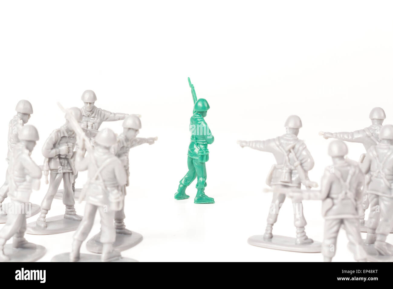 Gray toy soldiers pointing and bullying a green toy soldier Stock Photo