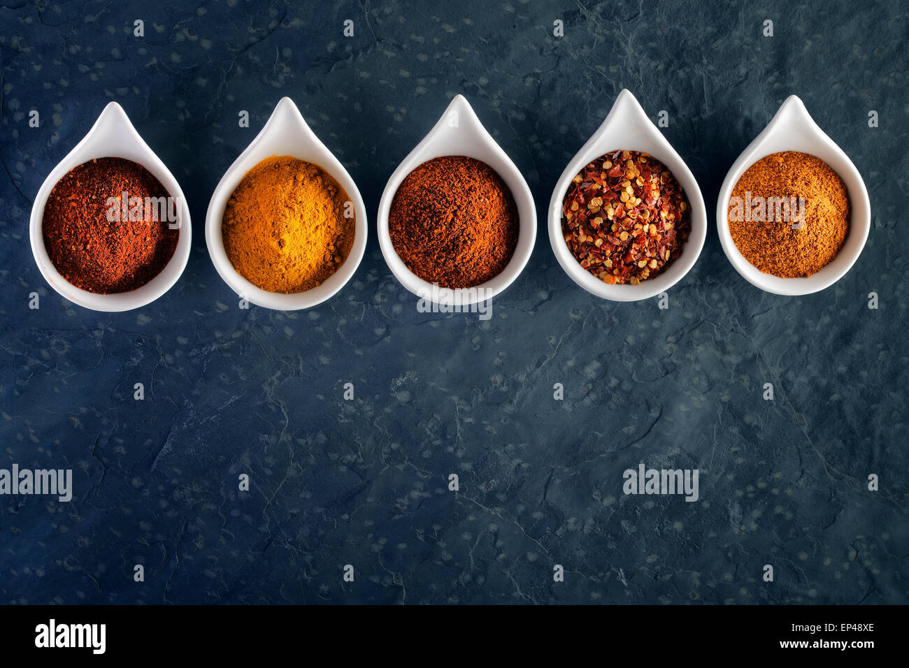Different spices in tasting spoons on dark slate from above Stock Photo