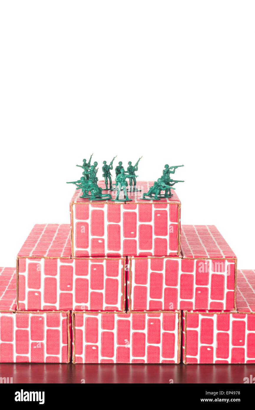 Green army men guarding the top of red cardboard brick base Stock Photo