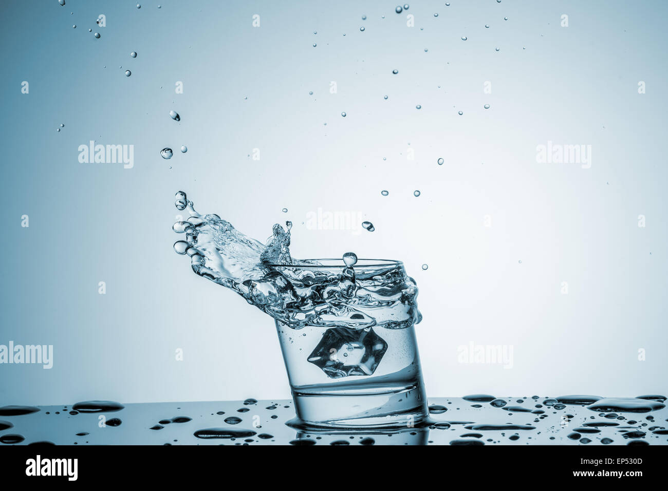 ice cube falling into a glass of water on blue background Stock Photo ...