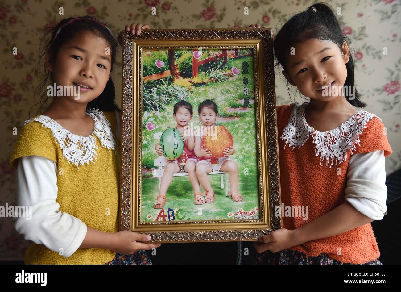 (150514) -- MOJIANG, May 14, 2015 (Xinhua) -- Twin sisters Jin Meixian (R) and Jin Huixian show a photo of four-year-old themselves in Mojiang Hani Autonomous County, southwest China's Yunnan Province, May 12, 2015.    Twin sisters Jin Meixian and Jin Huixian, 7, live with their mother Wang Fei, who opens a cold drink store. Their father does business in another province.    Meixian, the older, loves music and wants to be a musical teacher. Huixian likes dancing, and wants to go to college in Beijing. 'We always feel connected. Sometimes we find out that we are singing the same song, even the  Stock Photo