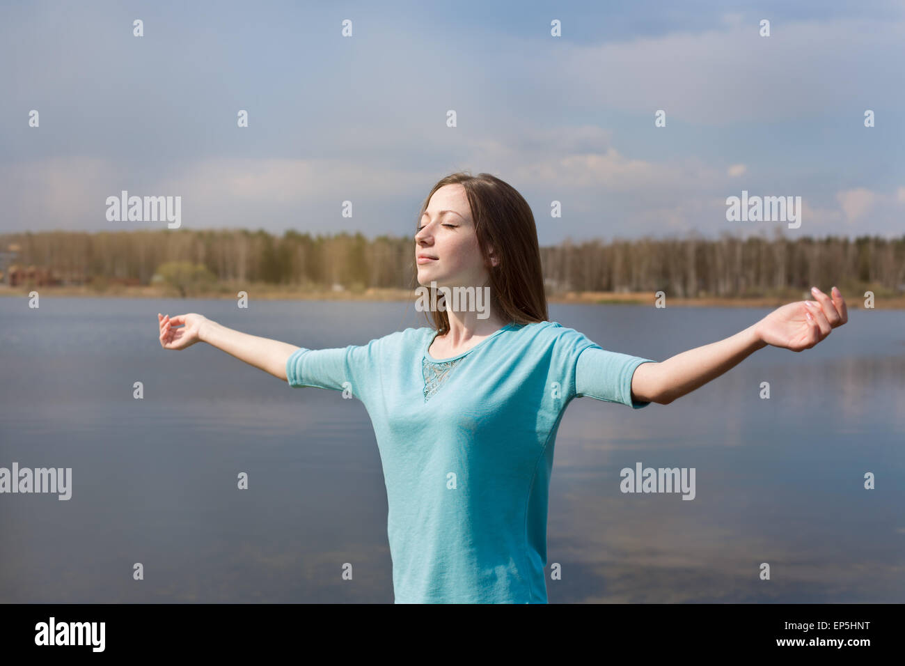 Happy girl with outstretched arms smiling to sun and closing his eyes Stock Photo