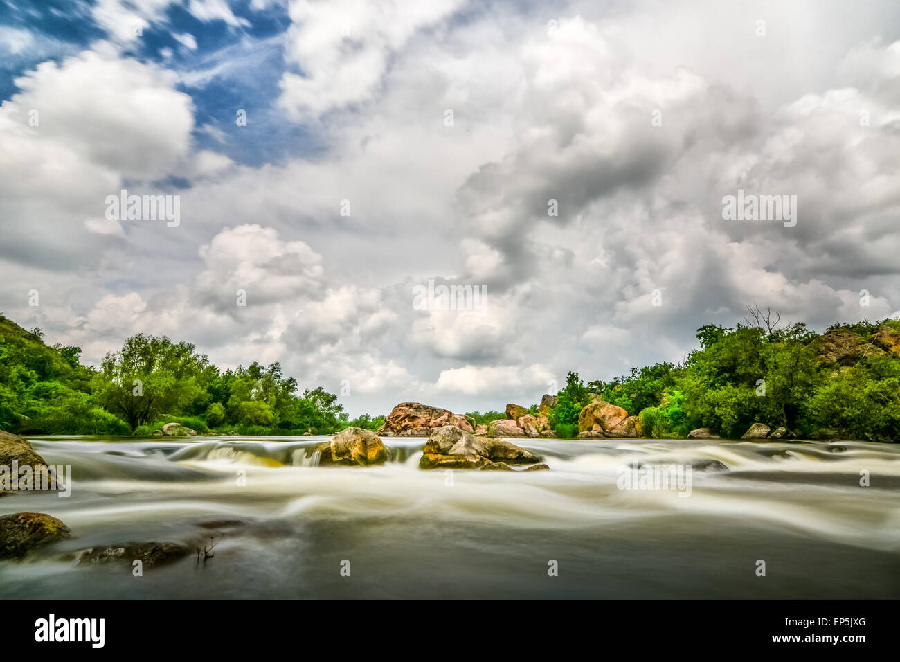 Beautiful river flow with sky stormy clouds, boulders in moving water - long exposure Stock Photo