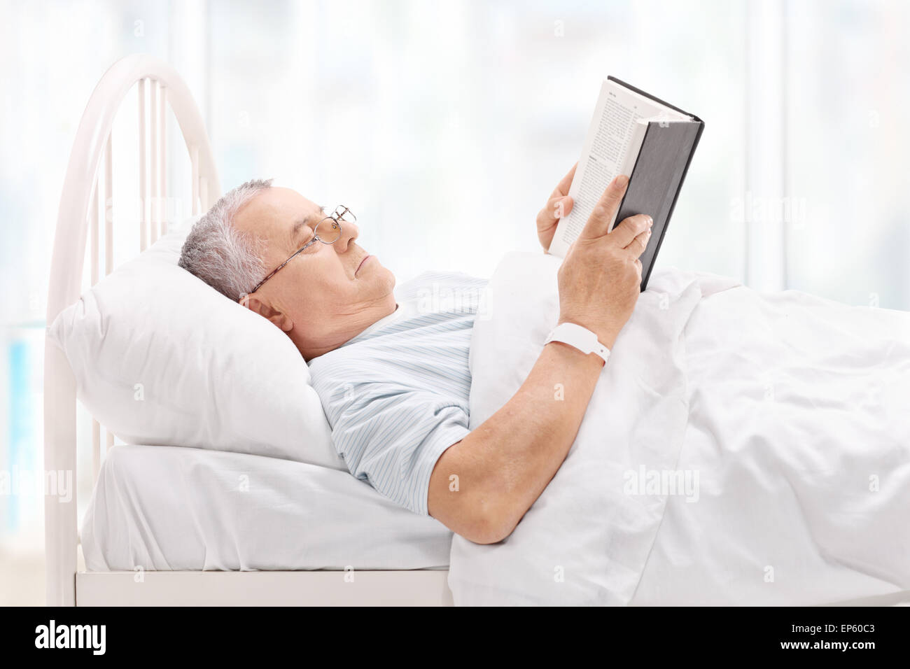 Mature patient lying in bed and reading a book in a hospital Stock Photo
