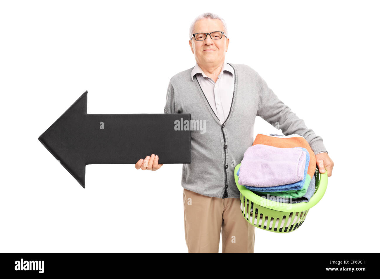 Senor gentleman holding a laundry basket full of clean clothes and a big black arrow pointing left isolated on white background Stock Photo