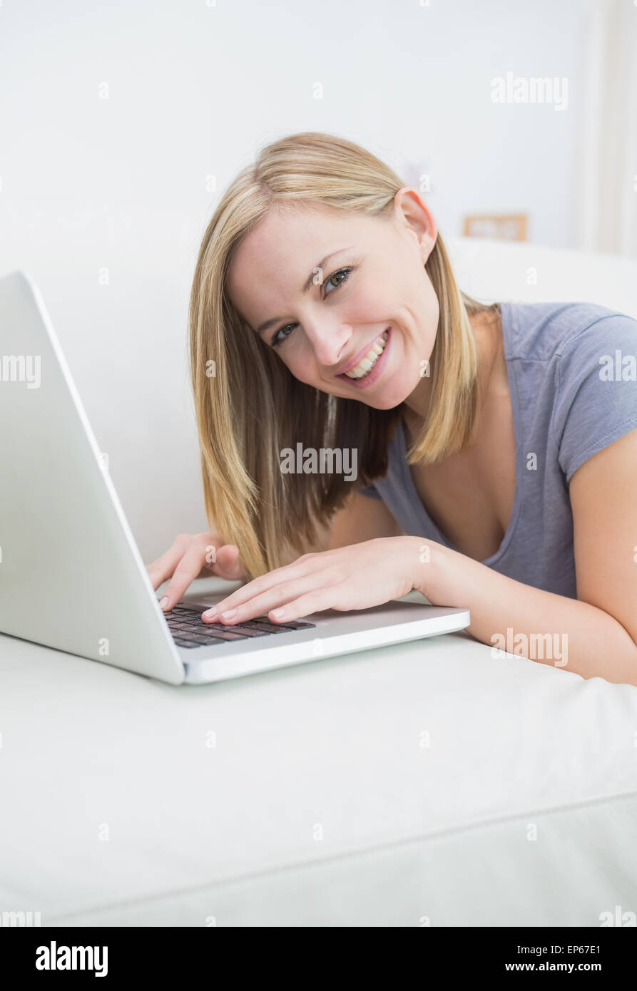 Portrait of casual woman lying on couch and using laptop Stock Photo ...