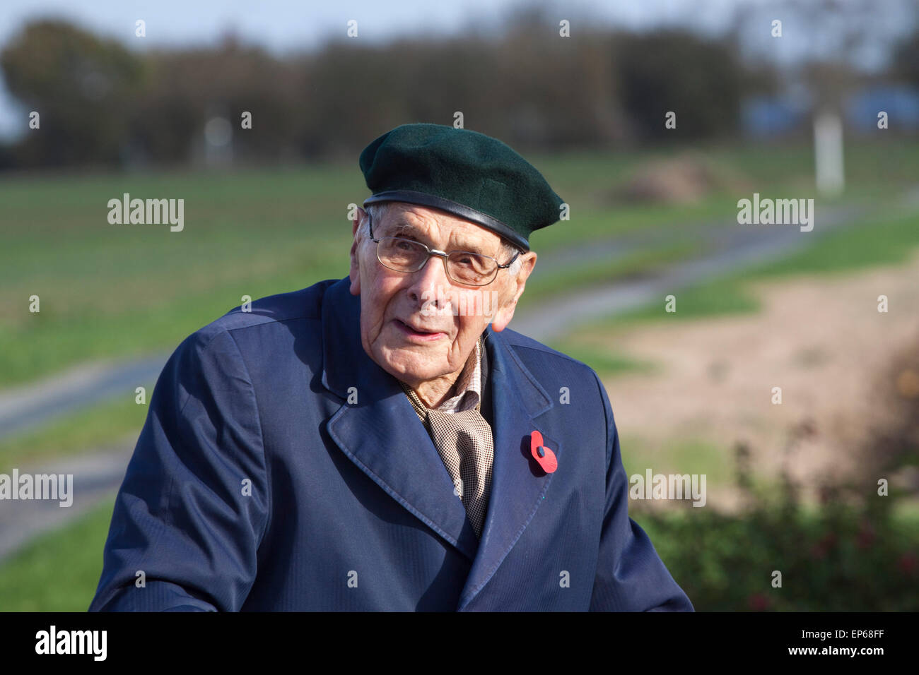 An elderly/senior man wearing a Remembrance Day poppy, beret and a blue raincoat Stock Photo