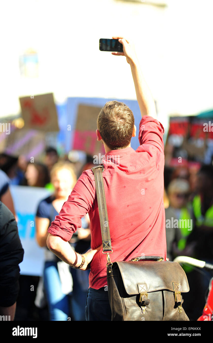 A man stops to take a photo with his camera phone as an anti-austerity protest passes. Stock Photo