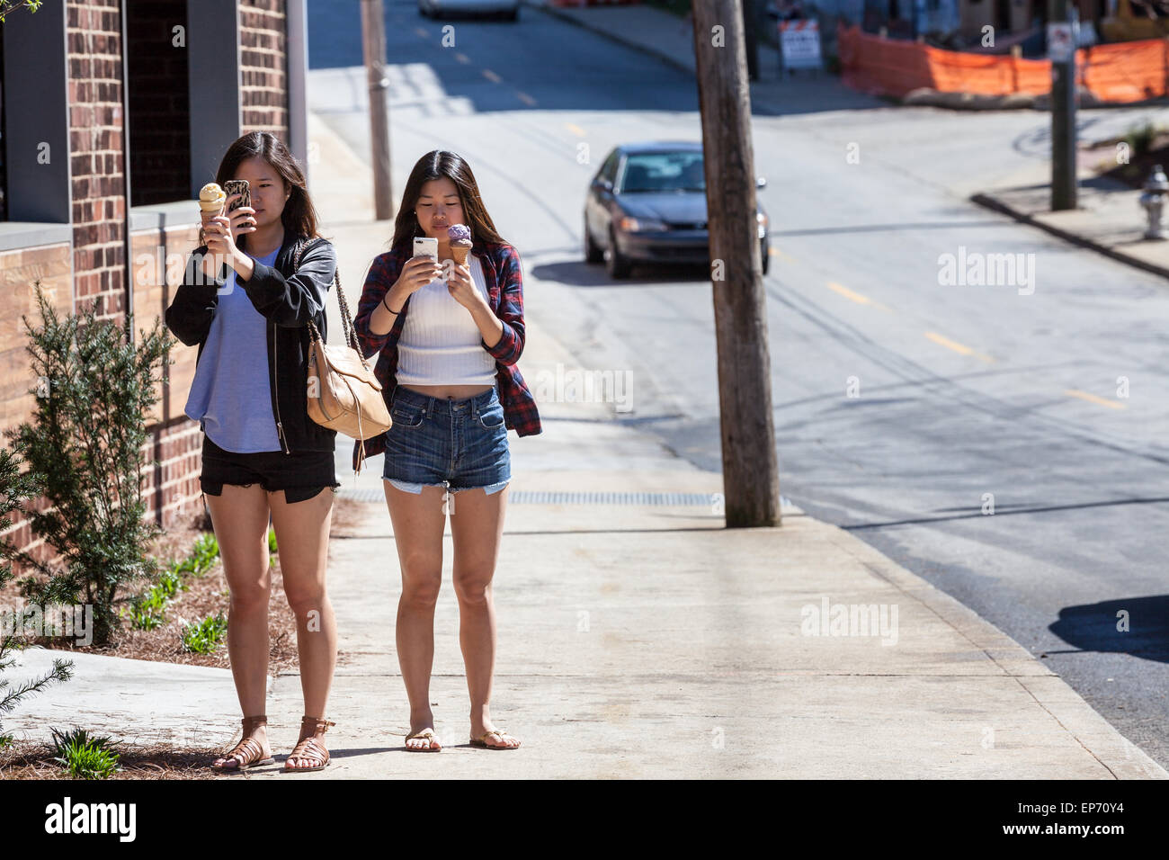 Two Asian-American women on ice cream cones and cell phones, Inman Park, Atlanta, Georgia, USA Stock Photo