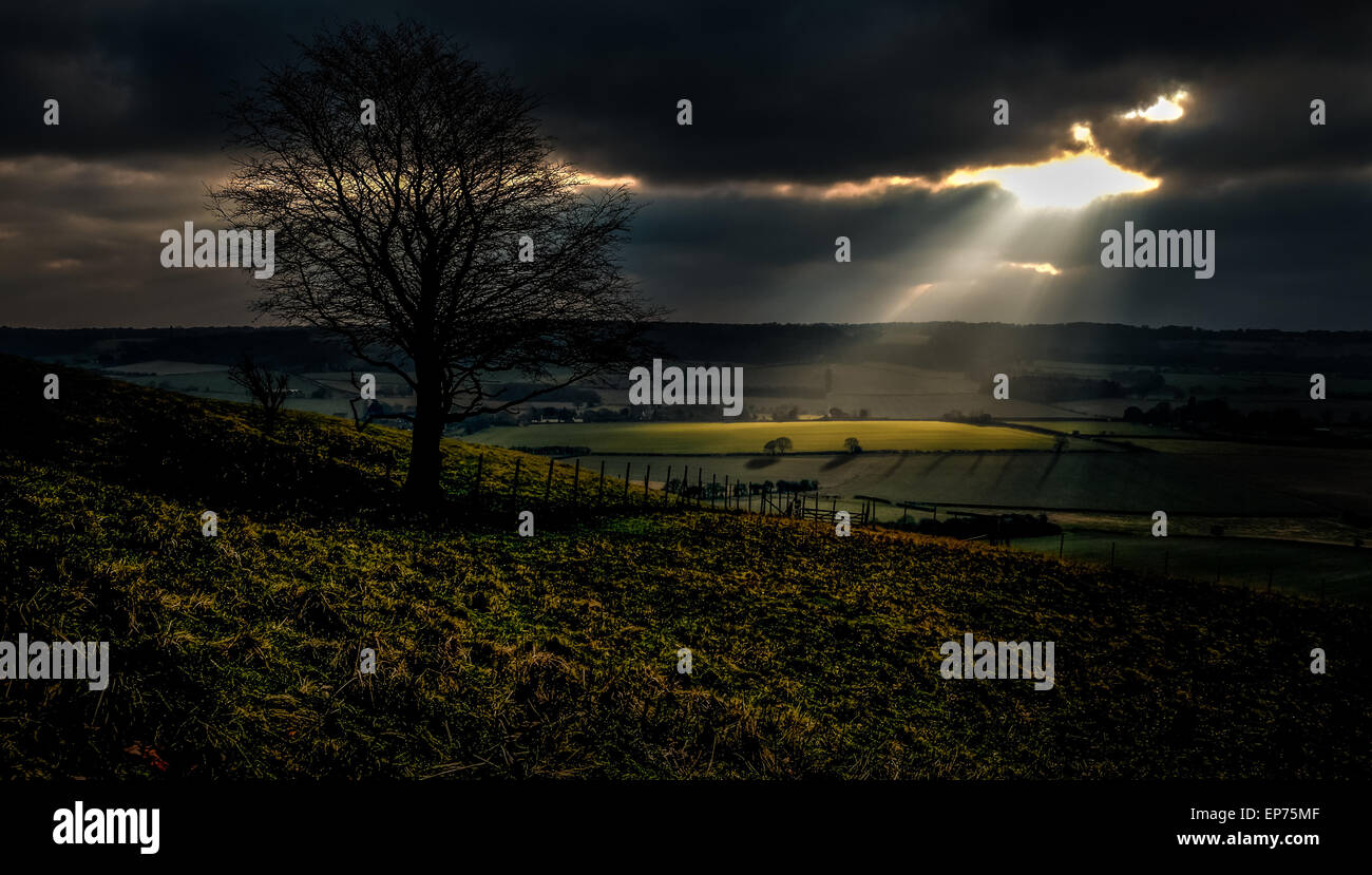 A Landscape view of the sun poking through the clouds lighting up the green fields Stock Photo
