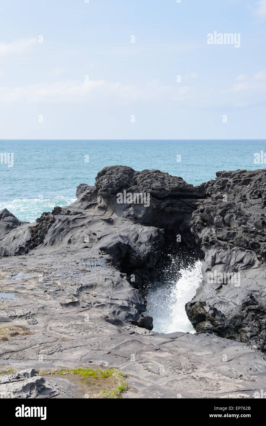 landscape with Spray of water by struck Seawater through tunnel between rocks at the coast near the Olle trail route 16  in Jeju Stock Photo