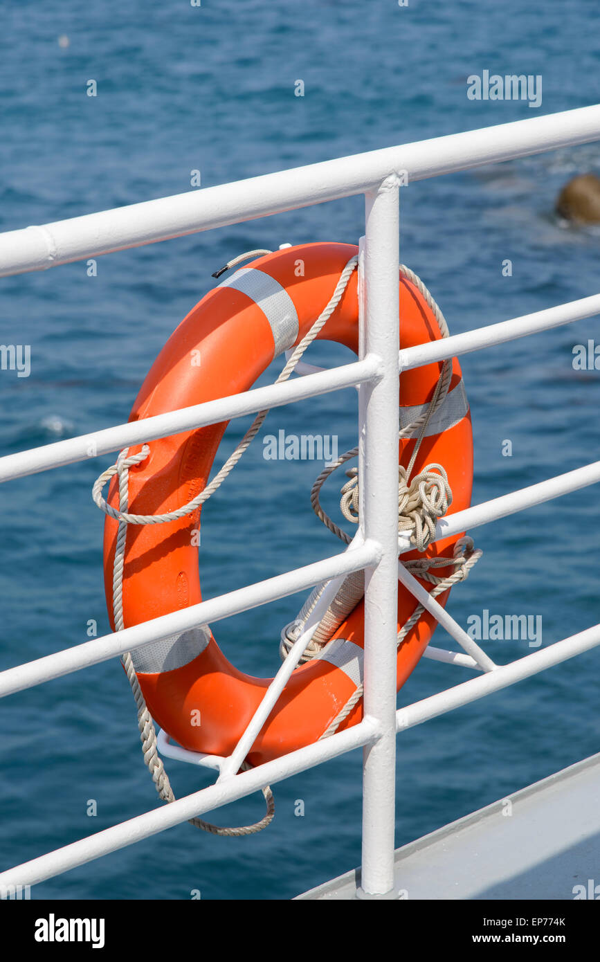 Orange colored lifebelt and rope hang on a white banister a passenger ship Stock Photo