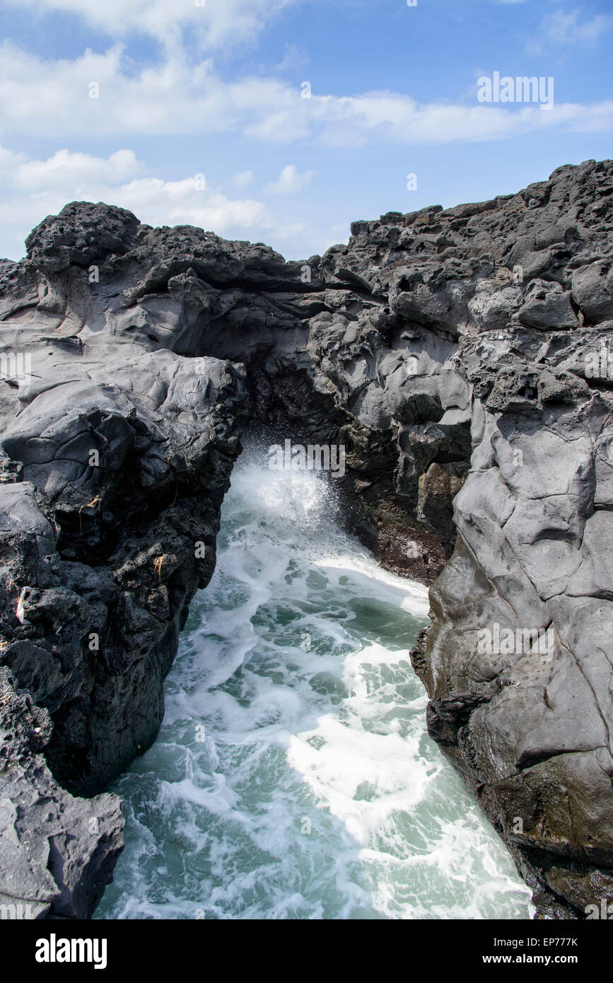 landscape with Spray of water by struck Seawater through tunnel between rocks at the coast near the Olle trail route 16  in Jeju Stock Photo